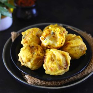 Side shot of aloo bonda on a black plate.