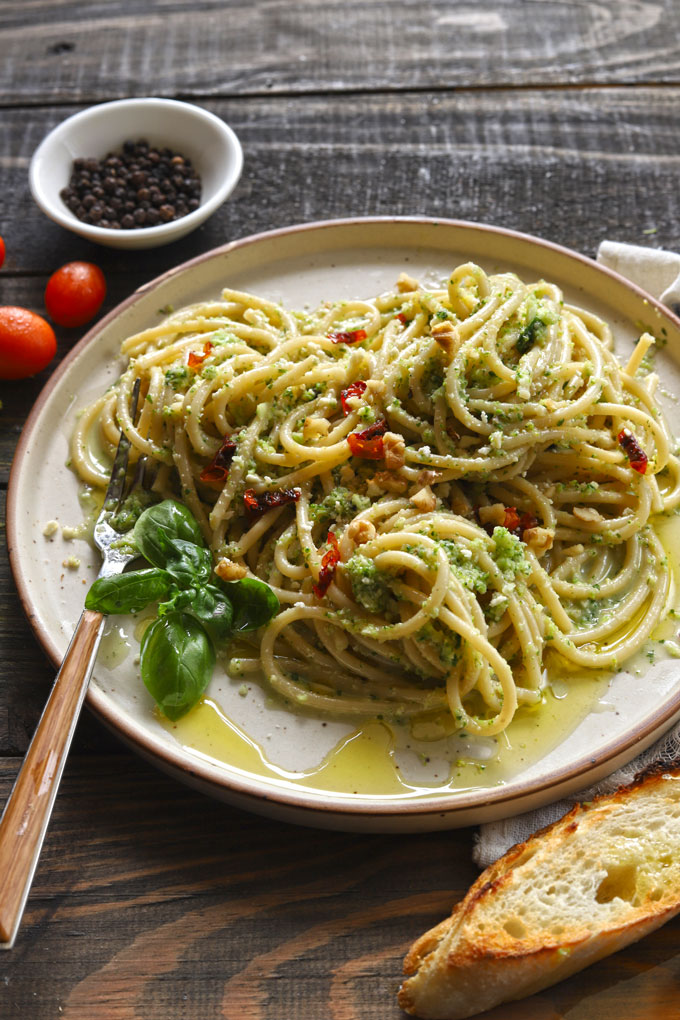 Side/aerial view of broccoli pesto pasta on wooden table with bread and tomatoes