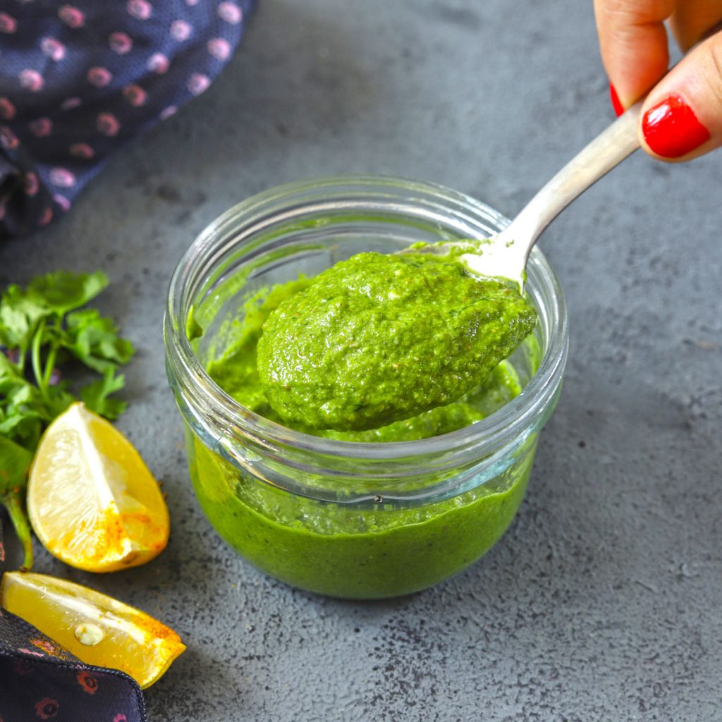 side close up shot of mint chutney in a glass jar with spoon scooping out the chutney