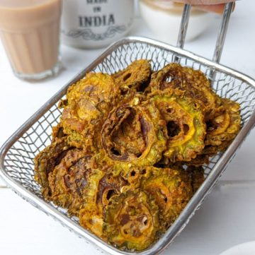 side shot of air fryer karela chips stacked on a wire basket