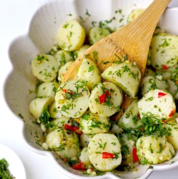 side angle shot of potato salad in a white ceramic bowl with the wooden spoon