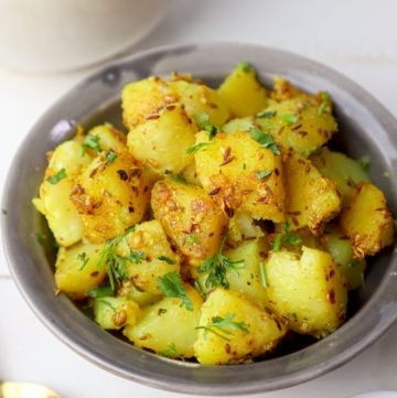 side close up shot of jeera aloo in a grey bowl