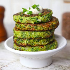 side shot of zucchini fritters stacked on a white plate